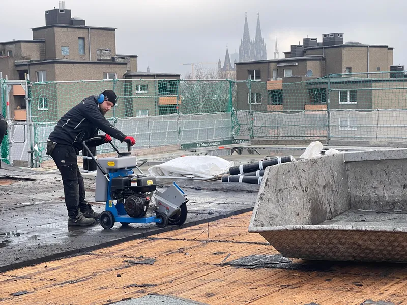 Dachdecker bei Arbeiten auf einem Flachdach, im Hintergrund der Kölner Dom.